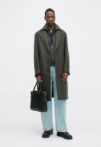 Garšs tumši zaļš mētelis ar griezuma apkakli, ar pogu aizdari, uzvilkts virs pelēka ar rāvējslēdzēju džempera. Gaismas zilo platās kājas bikses un melna soma.