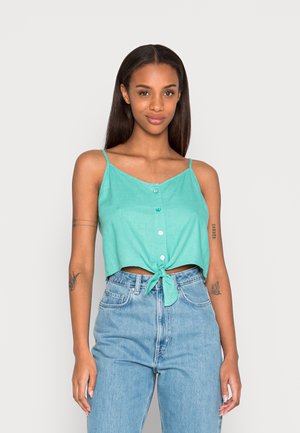 Top cropped turquesa com alças finas ajustáveis, fecho frontal com botões e bainha atada, combinado com jeans azul claro de cintura alta.