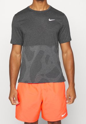 T-shirt Nike gris avec un motif texturé sur la moitié inférieure. Porté avec un short orange vif, ornés d'accents de logo Nike blancs.