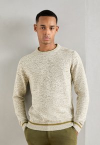 Lys beige strikket genser med et teksturmønster, rund hals og ribbede mansjetter. Hempen har en subtil grønn aksentstripe.