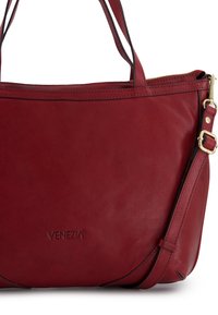 Red leather handbag with a smooth texture, zip closure, and dual carry straps. Features embossed logo and subtle curved accents.