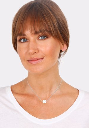 Sterling silver necklace featuring a floral pendant with four white petals, worn over a white shirt with a round neckline.