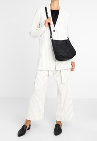 Blazer blanco con rayas finas y pantalones de pierna ancha, combinado con un bolso de hombro de ante negro y zapatos negros sin cordones.