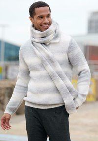 Hellgrauer Strickpullover mit strukturierten Streifen, kombiniert mit einem langen, leichten grauen Schal. Dunkle Hose vervollständigt das Outfit.