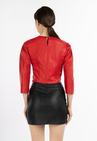 Piros műbőr crop top, háromnegyedes ujjakkal és hátul kulcslyuk részlettel, fekete műbőr mini szoknyával párosítva.