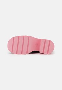 Semelle d'une chaussure rose avec des rainures épaisses horizontales et un petit logo embossé près de la zone de la voûte plantaire sur un fond blanc.
