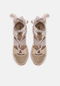 Vaaleanbeige urheilukengät, joissa on verkkomaiset paneelit ja satiinikoristeiset nauhat. Varustettu tekstuuripohjalla ja ristikkäisillä hihnoilla tukemiseen.