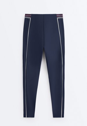 Colanți bleu închis cu dungi laterale albe și talie cu dungi orizontale roșii, albe și albastre.