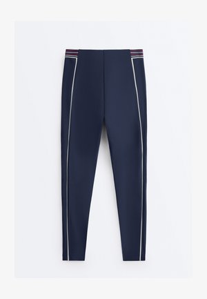 Tmavě modré legíny s bílými bočními pruhy a pasem s horizontálními pruhy v červené, bílé a modré barvě.