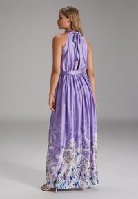 Abito maxi lavanda fluido con collo a halter e dettaglio a fiocco, caratterizzato da una stampa floreale sull'orlo e una vita elastica. Texture del tessuto liscia.