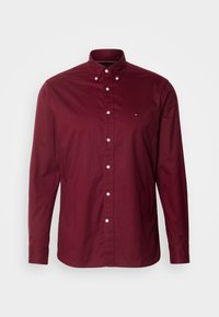Burgundowa koszula z długim rękawem, wykonana z bawełny, z klasycznym kołnierzykiem i białymi guzikami. Posiada małe logo na klatce piersiowej.