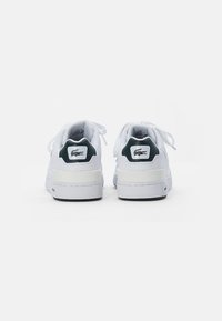 Białe skórzane sneakersy o gładkiej teksturze, z zielonymi akcentami na pięcie i białą podeszwą. Wyróżniają się sznurówkami oraz logo z tyłu.