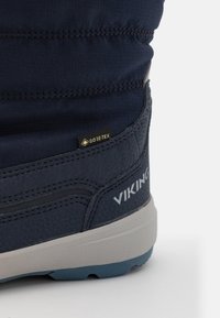 Kék bokacsizma bőrből és textilből, Gore-Tex címkével, strukturált felülettel és világosszürke talppal kék részletekkel.