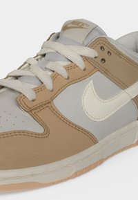 Близък план на бежово и сиво маратонка Nike с бели връзки и бяло лого на Nike отстрани.