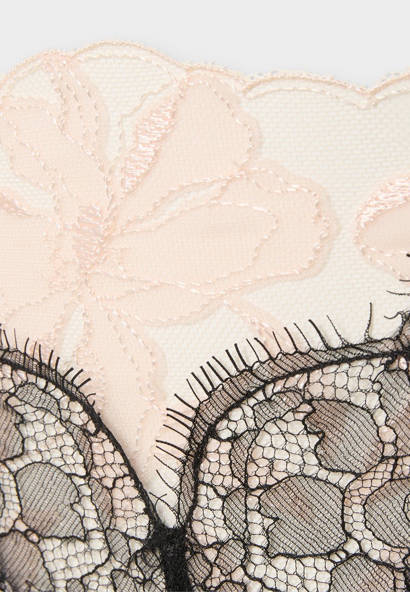 Delikat beige blonderstof med broderede blomsterprint og sort blonde med bølgede kanter og indviklet netmønster.