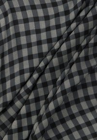 Μαύρο και γκρι ύφασμα με διαγώνιο καρό μοτίβο που περιλαμβάνει μαύρα τετράγωνα και υφασμάτινες γκρι διαμαντόσχημες μορφές, απαλά διπλωμένο.