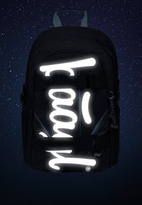 Zaino nero con design testuale riflettente bianco, caratterizzato da una superficie testurizzata, spallacci regolabili e una maniglia superiore.