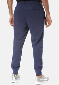Marinblå joggerbyxor i mjukt tyg, med avsmalnande ben, elastisk midja och en bakficka med dragkedja för förvaring.