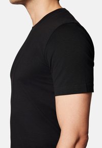 Czarny dopasowany t-shirt z krótkimi rękawami, wykonany z gładkiego materiału bawełnianego. Posiada okrągły dekolt i starannie wykończone brzegi.