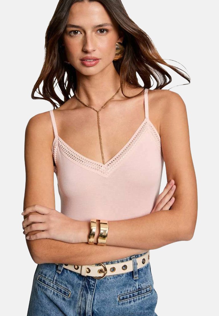 Débardeur rose clair avec des bretelles spaghetti réglables, présentant un décolleté en V et des détails en dentelle. Porté avec un jean en denim taille haute.