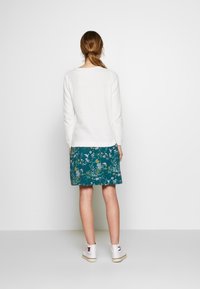 Biała bluzka z długim rękawem w połączeniu z turkusową spódnicą w kwiaty, charakteryzującą się luźnym krojem i miękką fakturą. Całość uzupełniają białe sneakersy.