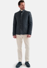 Gequilted zwarte jas met een hoge kraag, knopen aan de voorkant en een textuurpatroon. Draag het met crèmekleurige broeken en zwarte veterschoenen.