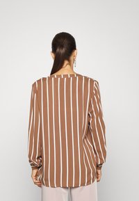 Blouse à manches longues rayée marron et blanche avec une coupe décontractée, un col rond et une texture douce, dotée de manches larges et tombantes.