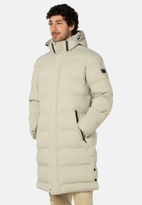 Beiger Steppmantel mit Kapuze, horizontal gesteppter Optik, Reißverschlusstaschen und schwarzen Akzenten. Midilänge mit lockerem Schnitt.