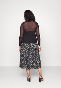 Top nero con schiena trasparente, abbinato a una gonna midi floreale con motivi verdi e neri. Scarpe con tacco chunky nere completano l'outfit.