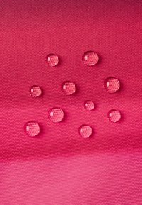 Vandafvisende stof i en gradient af pink med flere klare vanddråber på overfladen, der fremviser tekstur og vandafvisende egenskaber.