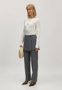 Witte lange mouwen top, grijze tailored broek met een gelaagd ontwerp en klep, puntige bruine hakken, met een beige clutch.