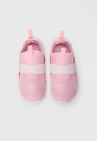 Des baskets Nike roses présentent un dessus en maille avec une texture lisse, des doubles boucles pour un enfilage facile, et une large sangle élastique au milieu du pied.
