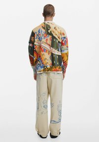 Strikket sweater med flerfarvede mønstre og ribbet tekstur. Kombineret med løstsiddende, cremefarvede bukser med blå illustrationer.