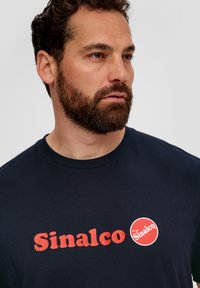 Marineblauwe katoenen T-shirt met vetrode "Sinalco" tekst en een cirkelvormig "Sinalco" logo. Gladde textuur, klassiek ronde halsontwerp.