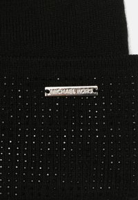 Czarna dziana czapka z wzorem fakturowanym i błyszczącymi metalicznymi akcentami. Zawiera srebrną metkę z logo z napisem "MICHAEL KORS".