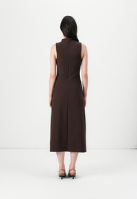Brun ärmlös klänning med en åtsittande bodice och midi-längd, med hög halsringning och en rak silhuett. Enkelt design, slät textur.
