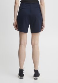 Marineblauwe shorts met een hoge taille en een gladde textuur, voorzien van een achterste ritssluiting en zijzakken, gecombineerd met zwarte hoge sneakers.