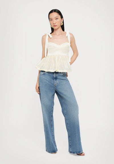 Top blanco de peplum con tirantes ajustables y un corsé entallado, combinado con unos vaqueros de pierna ancha de cintura alta en un tono azul claro.