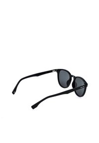 Lunettes de soleil noires à monture ronde avec verres foncés et branches fines, vues sous un angle arrière trois quarts sur fond blanc.