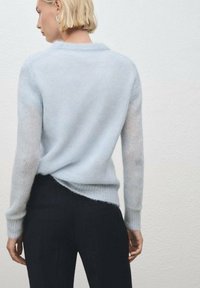 Pullover azzurro chiaro e peloso con scollo rotondo e maniche lunghe, abbinato a pantaloni a righe scure, visto da dietro su uno sfondo neutro.