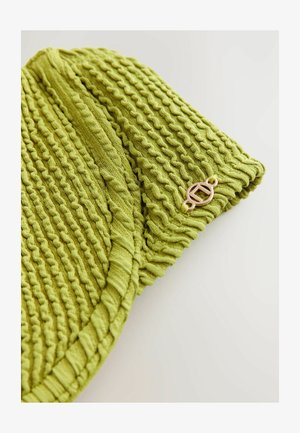 Roheline kudumine beanie, millel on tekstuuriga, laineline muster. Küljel on väike kuldne logo. Pehme materjal ja ribaga ääred.