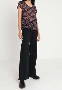 Pantalons noirs à jambes larges avec une texture lisse, associés à un haut à manches courtes à motifs présentant des designs géométriques en bordeaux et en rose pâle.