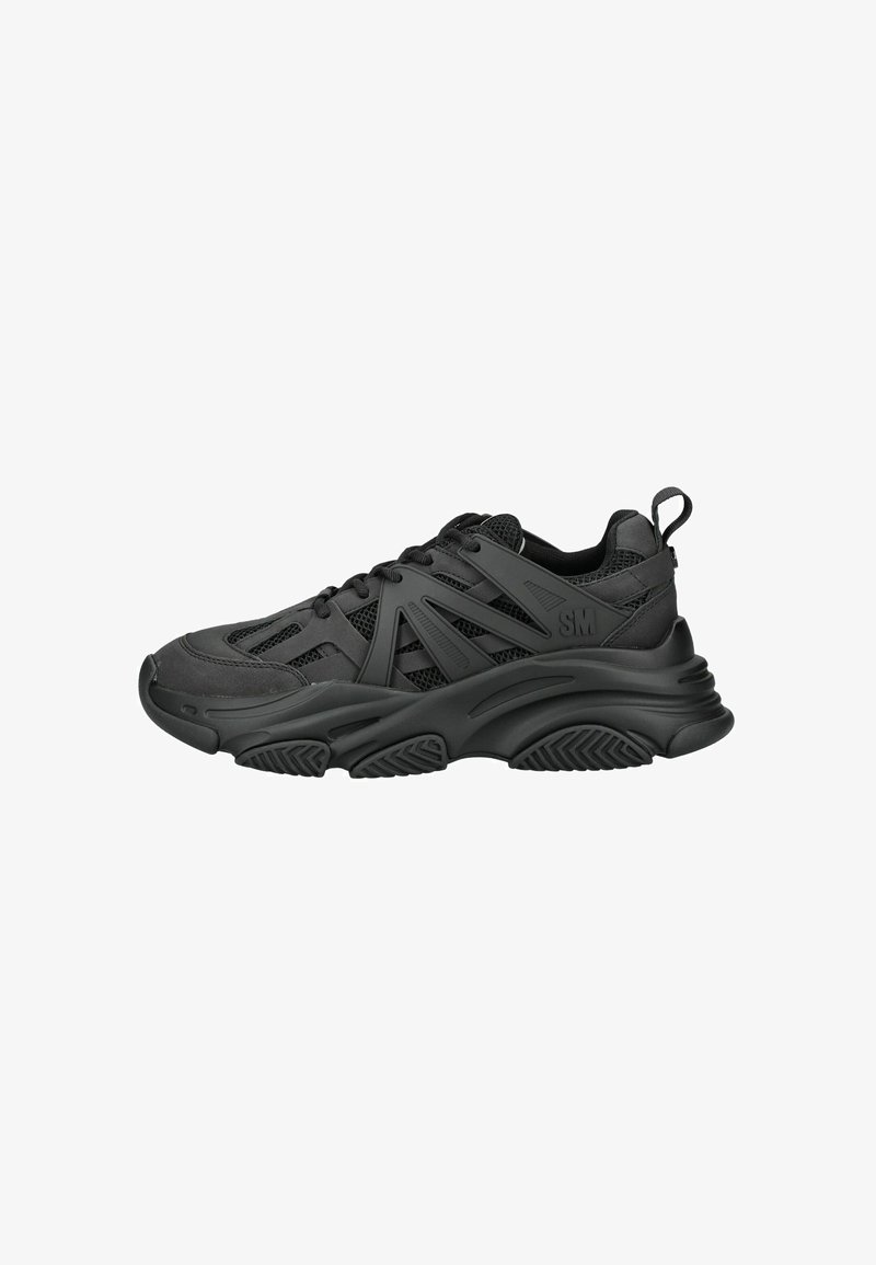 Zapatillas deportivas negras con parte superior texturizada, que presentan paneles de malla, suela de goma gruesa y un patrón de banda de rodadura prominente. El diseño incluye cordones y una pestaña en el talón.