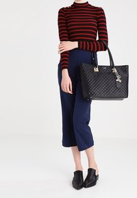 Schwarze gesteppte Handtasche mit silbernem Zubehör, getragen mit einem rot-schwarzen gestreiften Oberteil und Navy-Culottes. Schwarze Slipper.