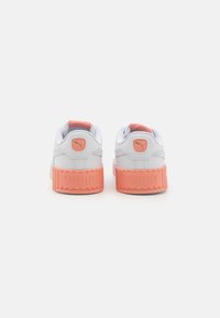 White sneakers with pink accents, layered rubber soles, and a padded collar, featuring a logo on the back and textured detailing.