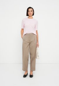 Ανοιχτό ροζ πλεκτό τοπ με κοντά μανίκια και σχέδιο ρόμβου, συνδυασμένο με ανοιχτό καφέ παντελόνια φαρδιάς γραμμής και μαύρα φλατ παπούτσια. Συμπληρώνεται με λευκή τσάντα.