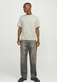 Lys grå kortærmet t-shirt med afslappet pasform, parret med løst siddende blå denimjeans. T-shirten har et lille logo på brystet.