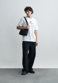 Black quilted shoulder bag with a strap, paired with a white T-shirt and loose black pants. Simple design with minimal hardware accents.