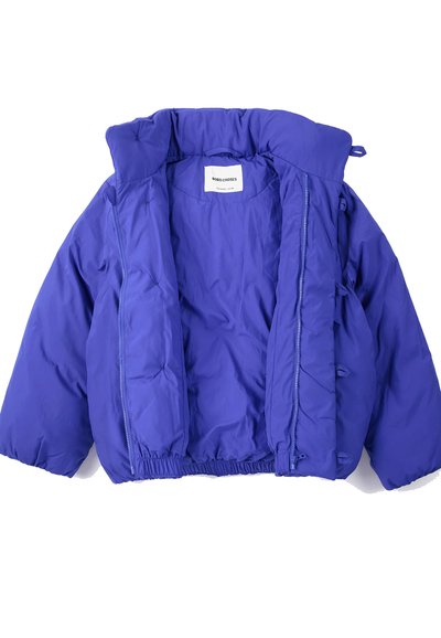 Veste matelassée bleue avec col montant, fermeture éclair avant partiellement ouverte, bas élastiqué et étiquette à l'intérieur de l'encolure.