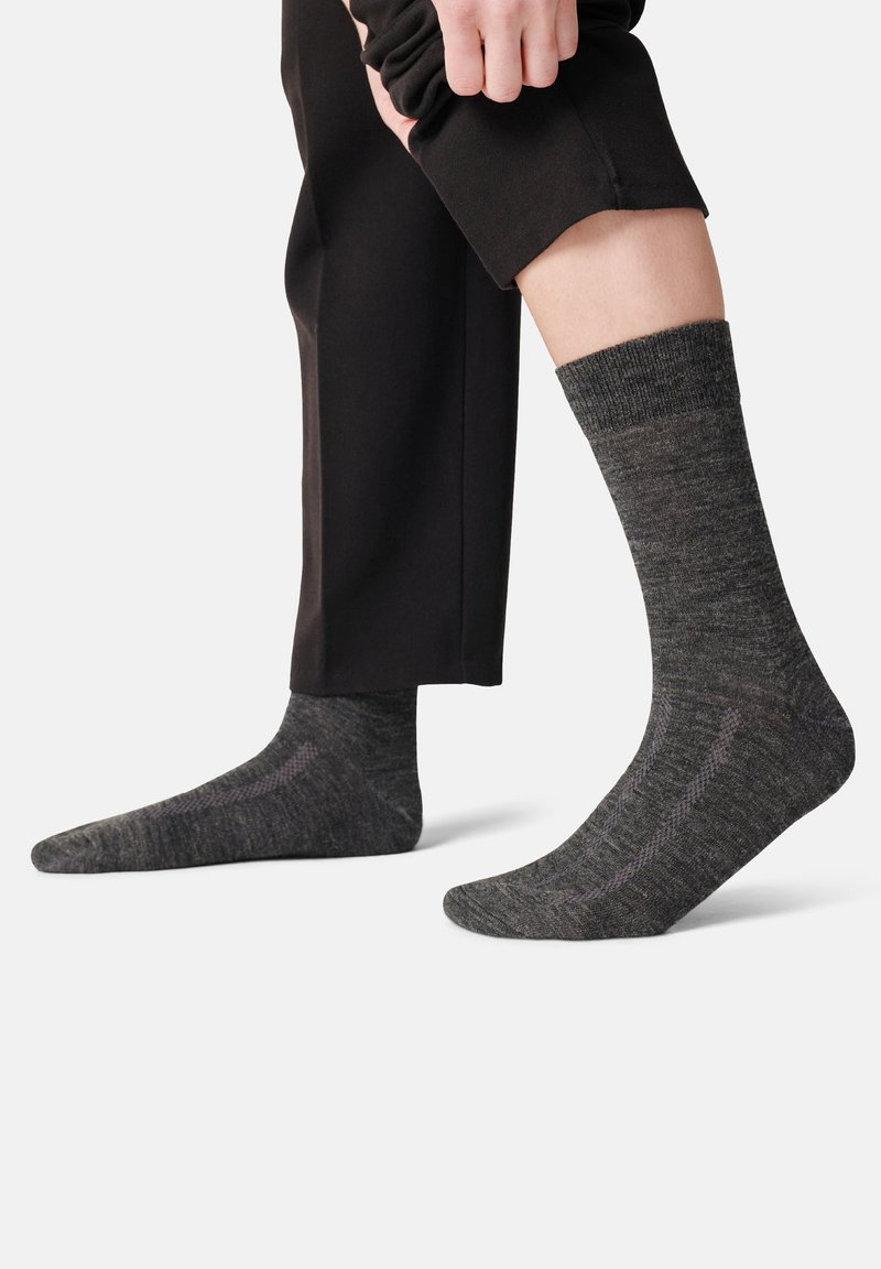 Mörkgrå strumpor gjorda av ett strukturerat material, med ribbade manschetter och subtila mönster längs sidorna. Bärs med svarta byxor.